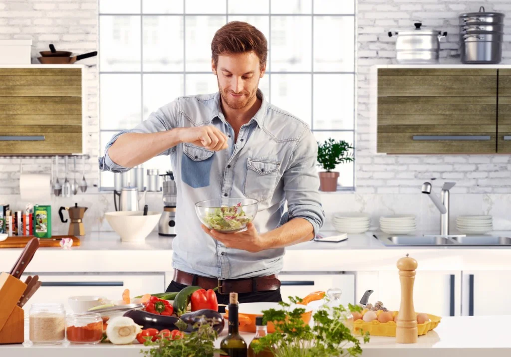 Bel homme cuisinant à la maison préparant une salade dans la cuisine.